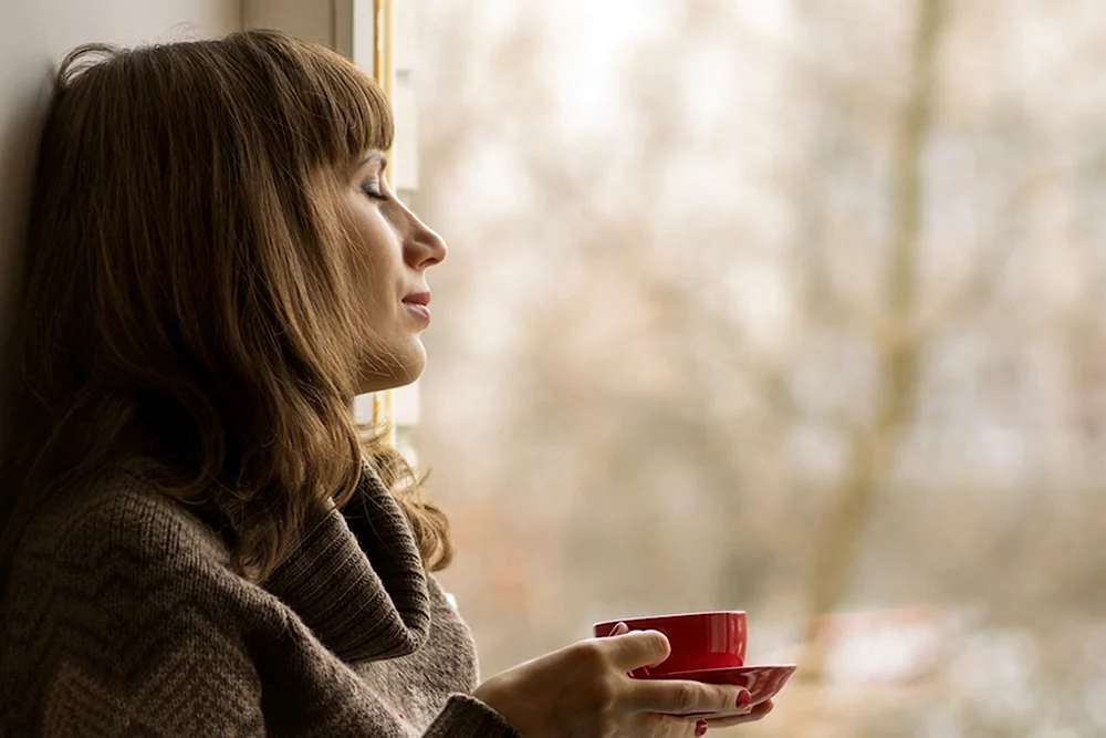 Девушка за окном с чашкой кофе